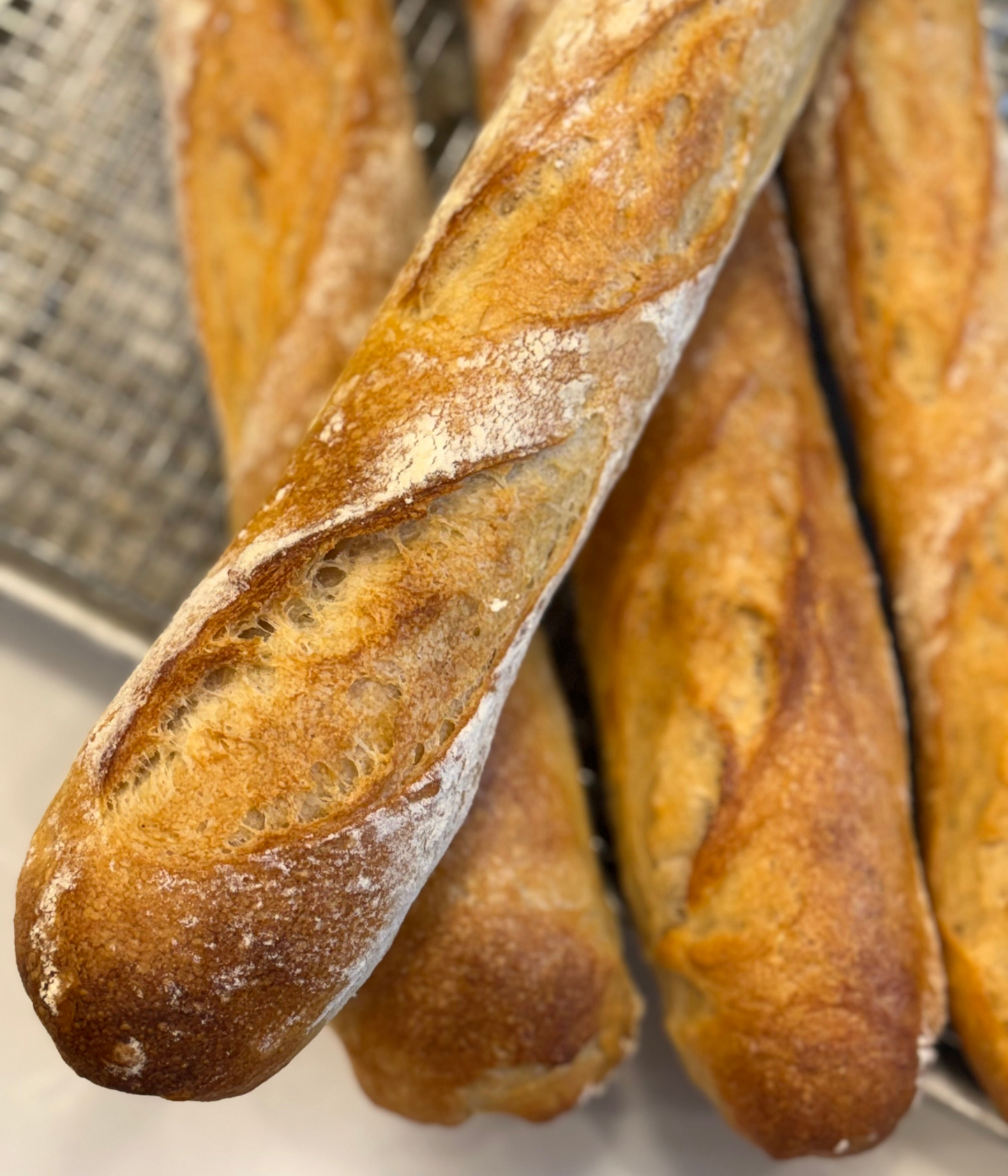 Close-up of freshly baked Crescent Bakes baguettes with a metal basket in the background.