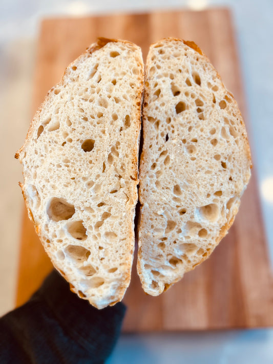 A freshly baked Crescent Bakes bread loaf cut in half, showing the inner texture, on a wooden cutting board.
