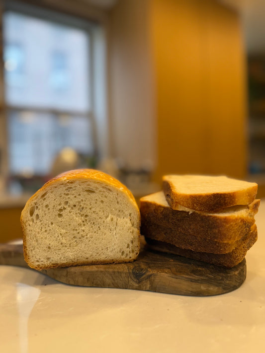 A loaf of Crescent Bakes Sandwich bread with slices cut and stacked on a wooden cutting board in a kitchen.