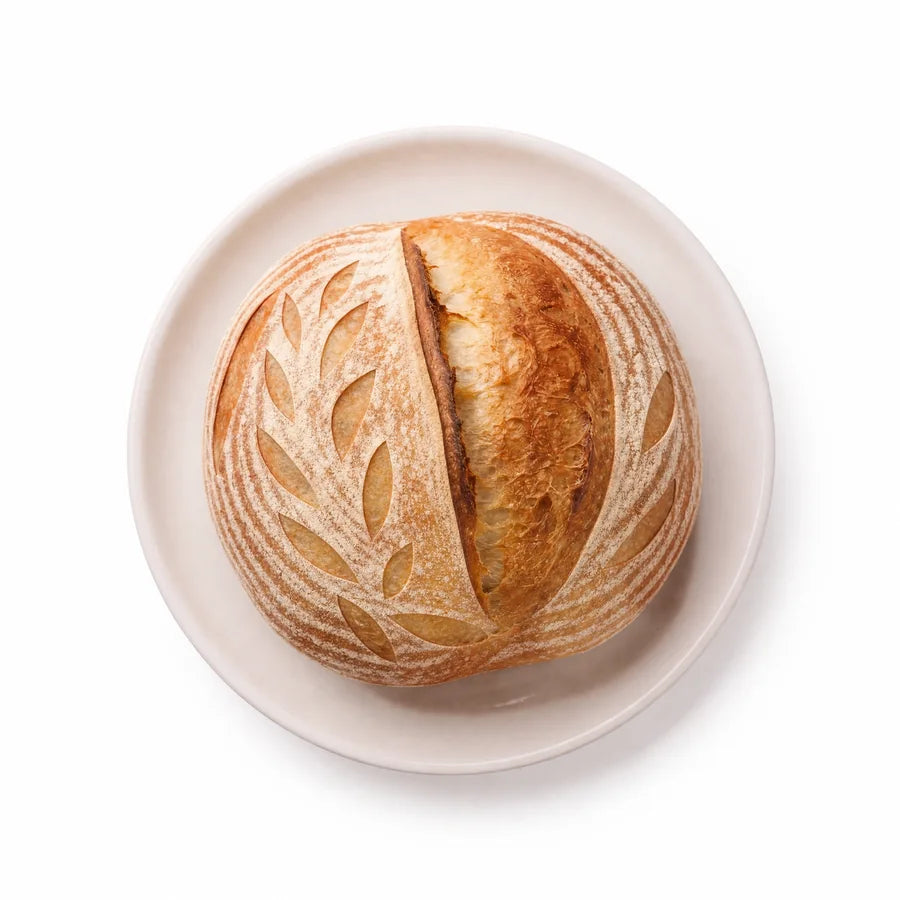 A freshly baked Crescent Bakes Sourdough Bread loaf on a wooden cutting board with a blurred kitchen background.