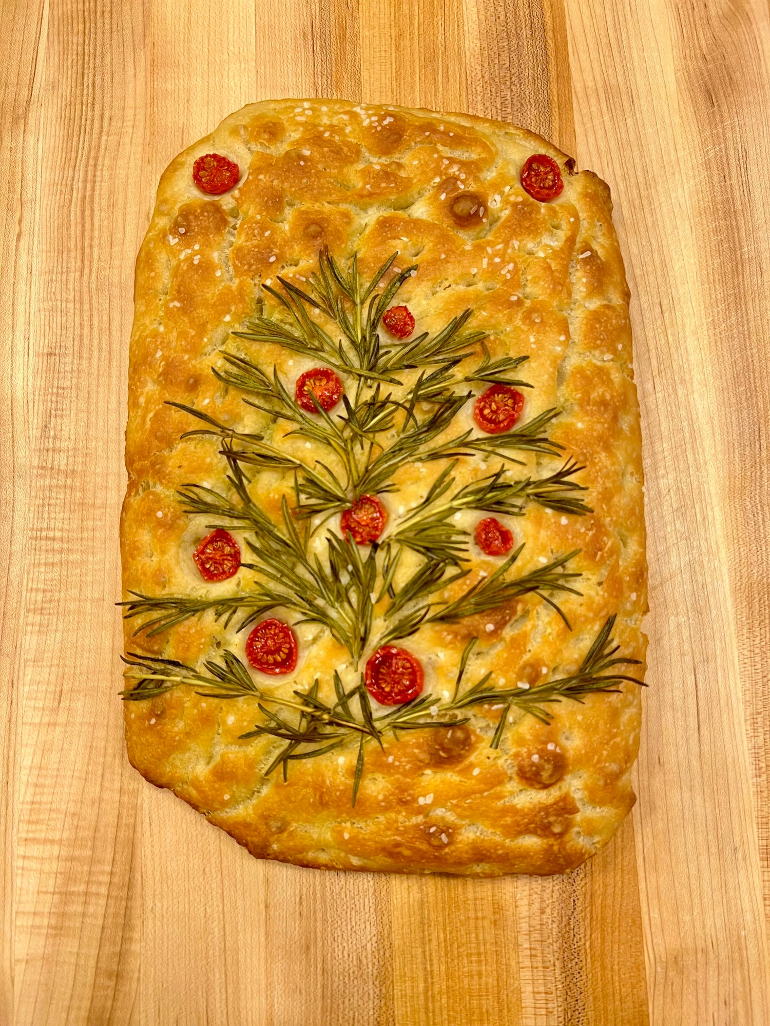 A freshly baked Crescent Bakes Focaccia bread with olive oil and herbs on a wooden surface.