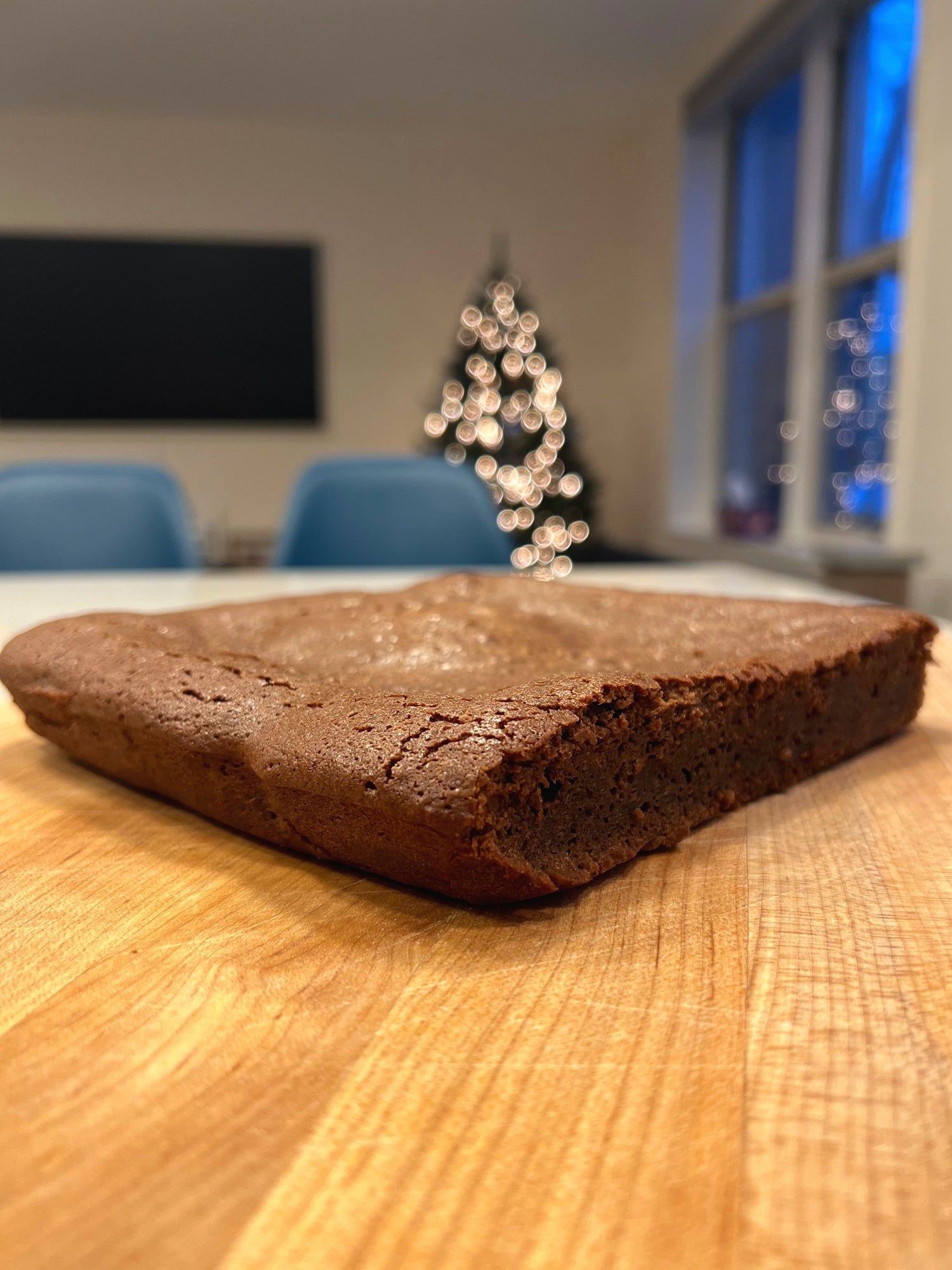 A Fondant au Chocolat on a wooden surface with a blurred background featuring blue chairs and a decorated Christmas tree.