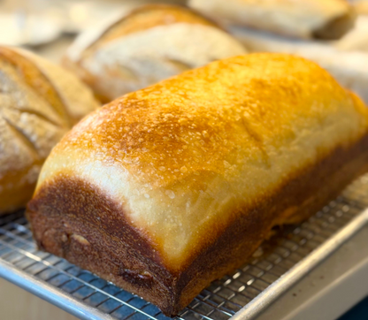 Loaf of Crescent Bakes Sandwich bread on a cooling rack with other bread items in the background
