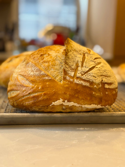 A loaf of Crescent Bakes Sourdough Bread on a cooling rack with a blurred background