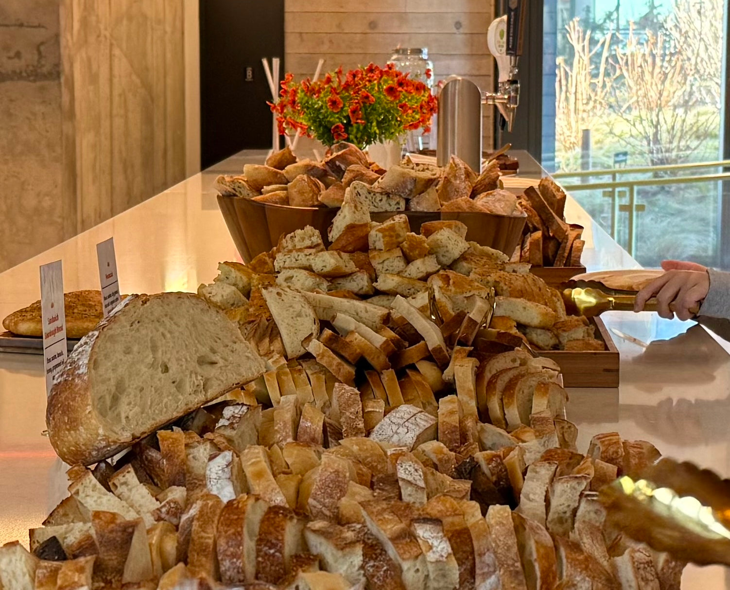 Assorted bread display on a table with a decorative flower arrangement in the background.